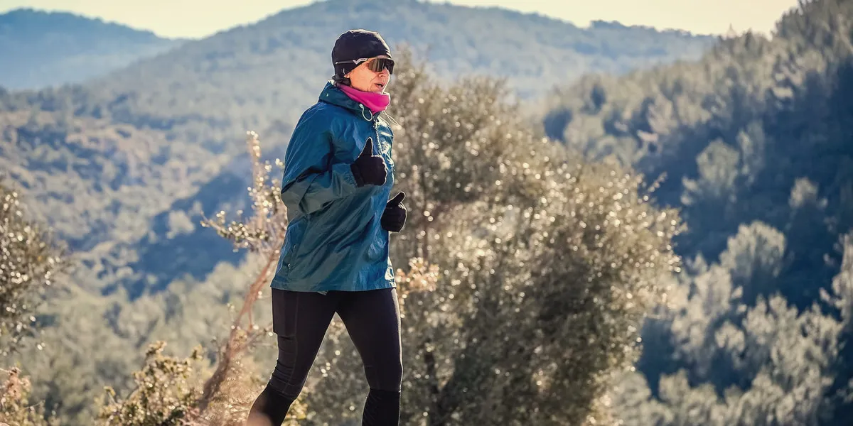 Ältere Frau beim Wandern vor bewaldeten Hügeln