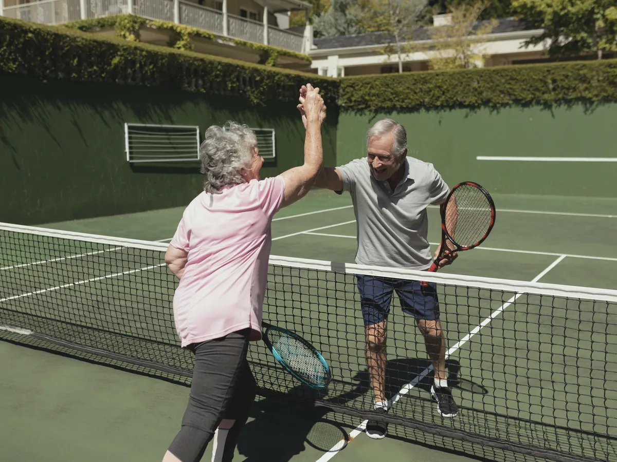 Älteres Paar gibt sich beim Tennis über dem Netz ein High-Five